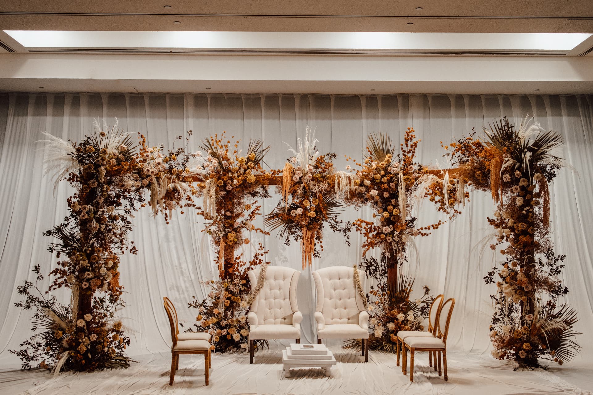 Indoor stage with white drapery, dried florals and two white lounge chairs