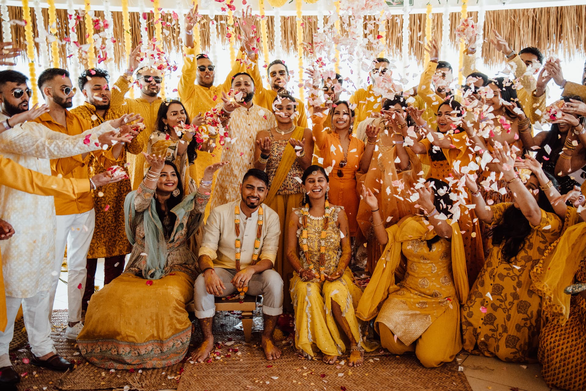 Divya and Harsh surrounded by guests throwing flower petals during the Haldi