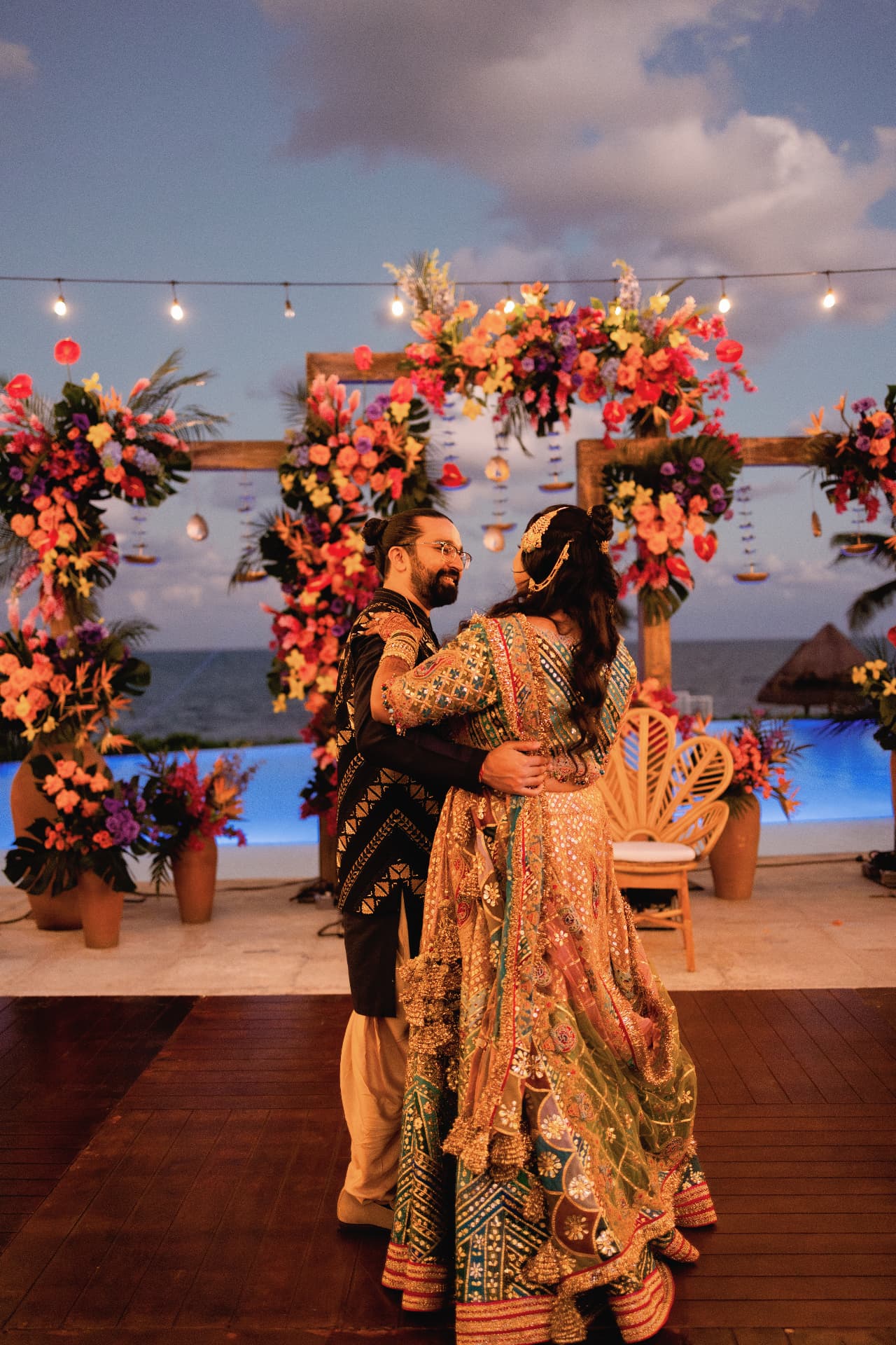 The couple dancing beneath vibrant floral décor and string lights