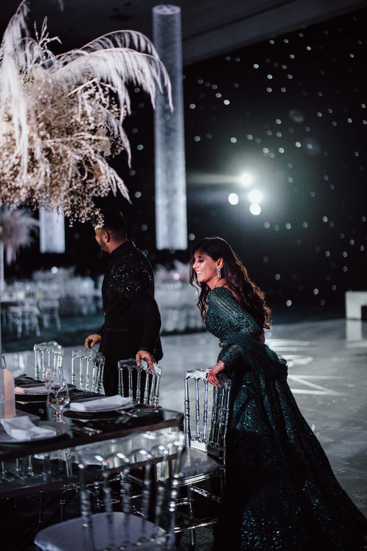 The couple beside a dark tablescape under floral décor and lights