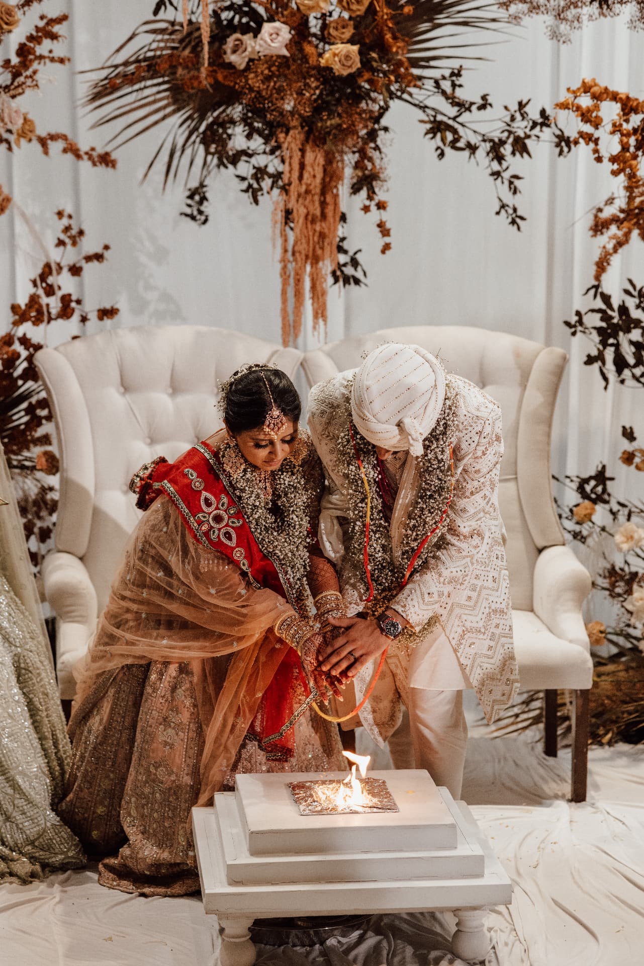 Divya and Harsh seated together in traditional attire during a ceremony ritual
