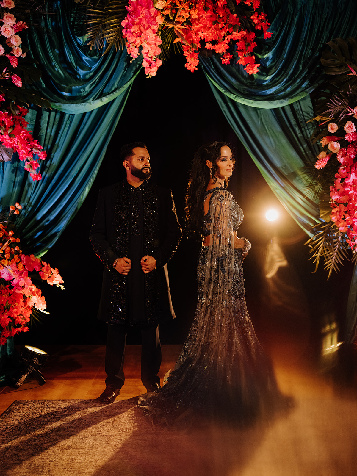 Sneha and Apoorv framed by teal drapery and red flowers