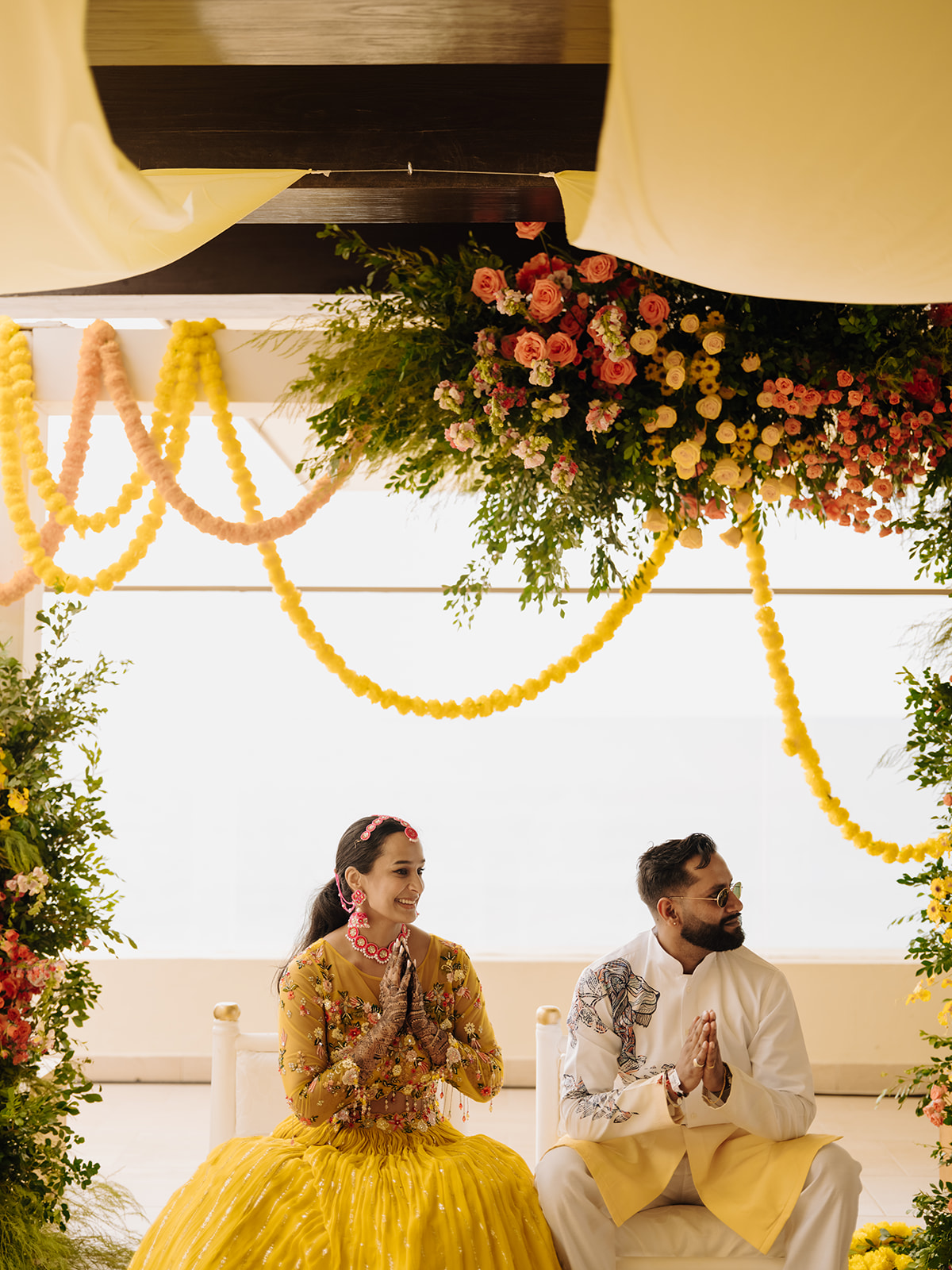 Sneha and Apoorv seated beneath yellow garlands