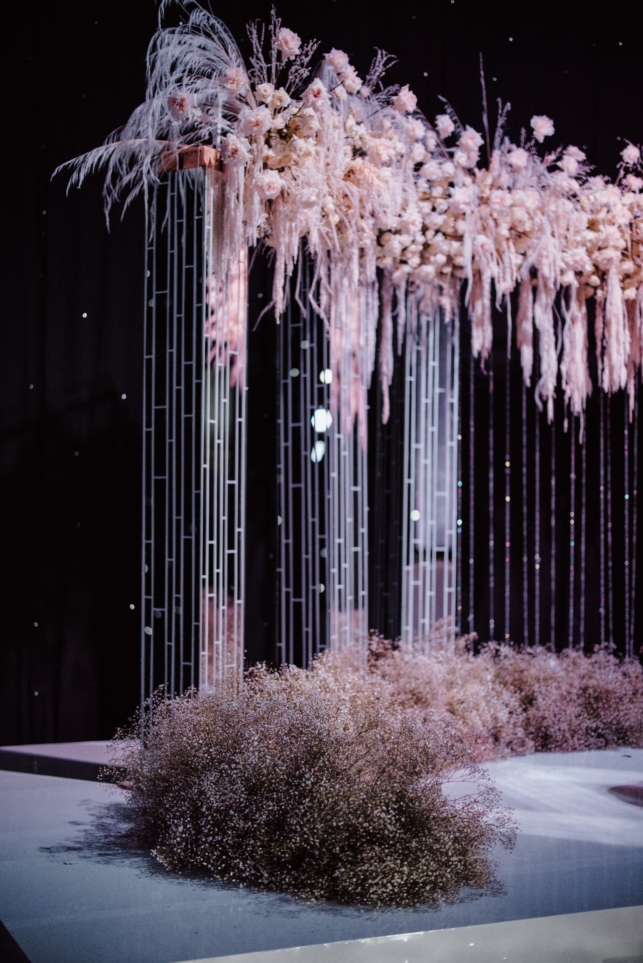Floral installation at night with pale pink flowers and pampas grass