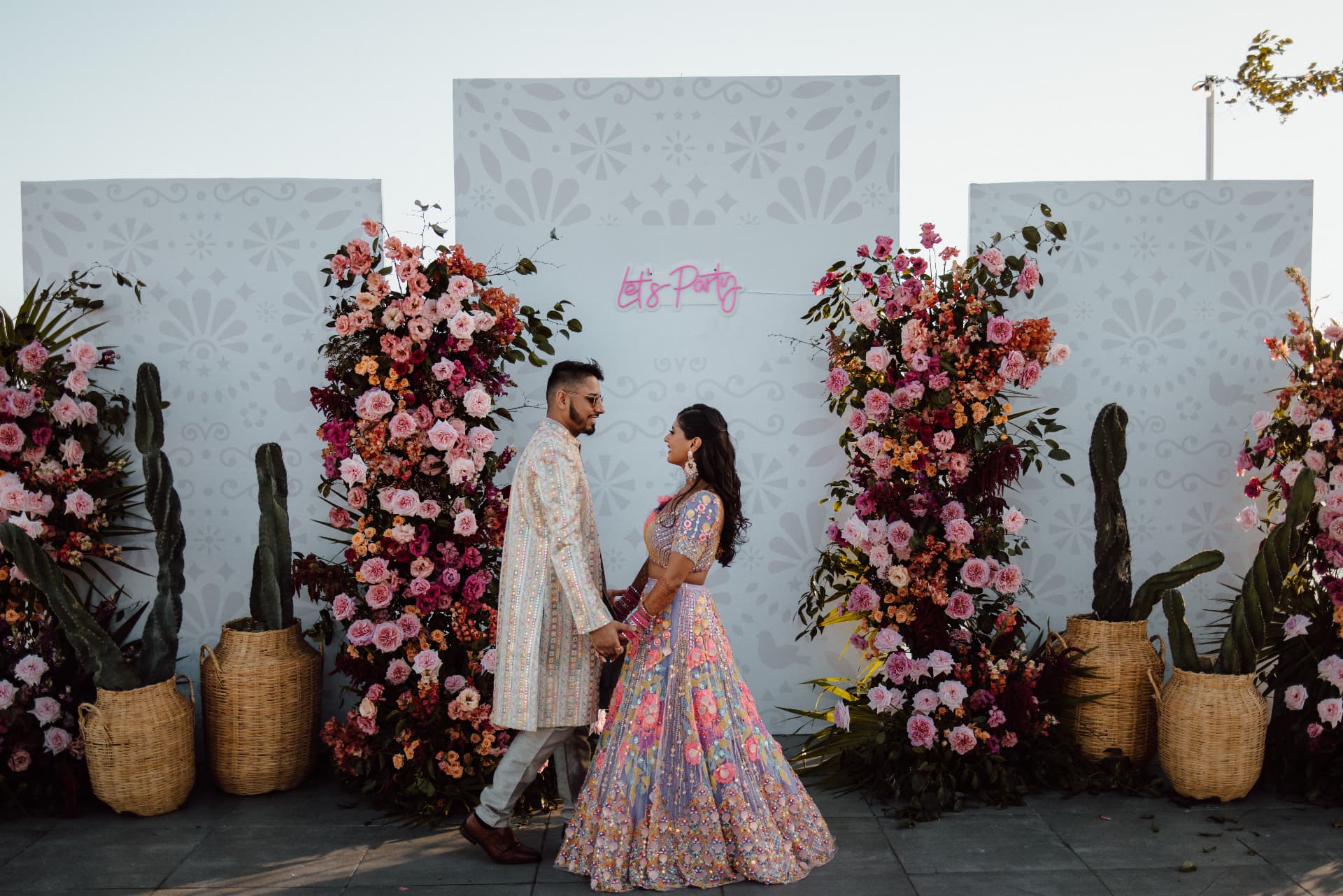 Divya and Harsh walking between large pink floral installations