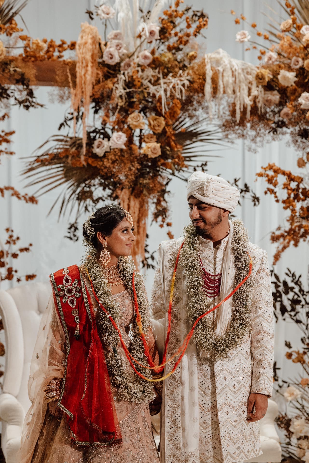 Newlywed couple beneath an architectural floral ceremony installation