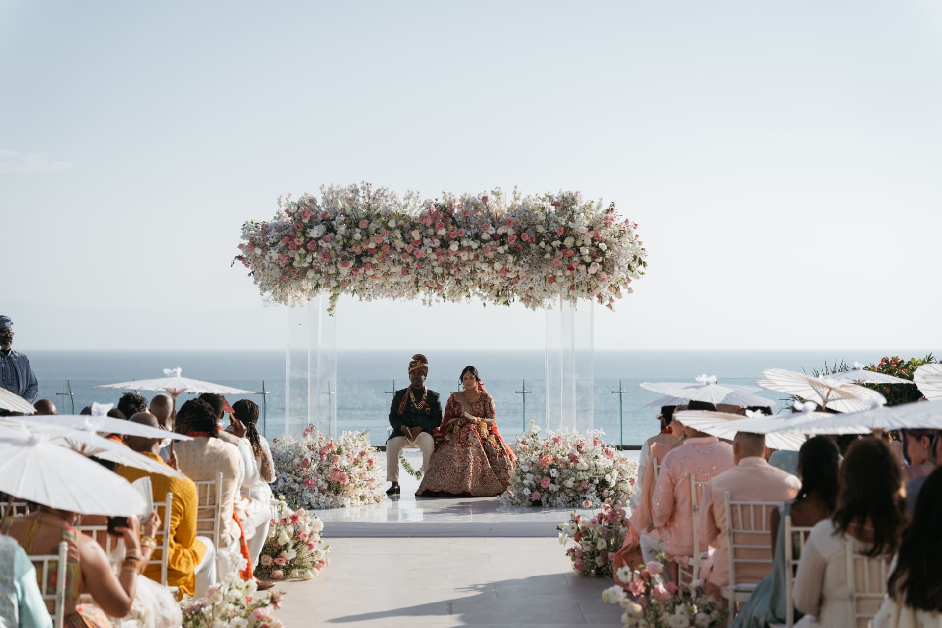 Cynthia and Azriel seated beneath an oceanfront floral canopy